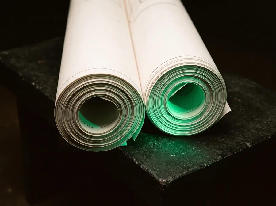 Two rolled drawing sets on a dark bench, emerald light glowing inside the spiral